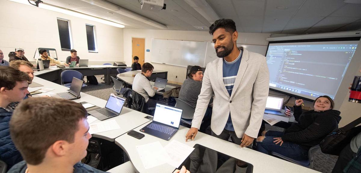 A Computer and Information Sciences professor stands amongst students working in a computer lab while giving instructions.