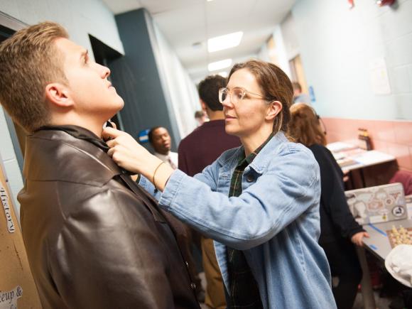 Photo of crew member helping student with costume backstage