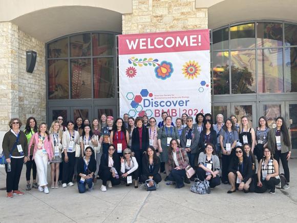 The 2024 Discover BMB Biochemistry Conference in San Antonio. A large group of people pose and smile in front a large white, pink, and blue poster which reads, "Discover BMB 2024". 