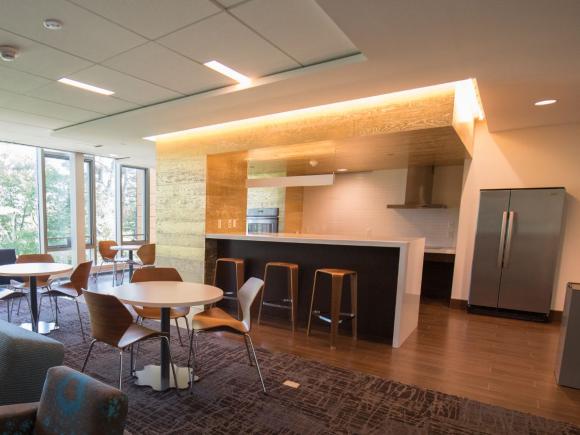 A communal kitchen, lounge, and dining area in University Hall featuring a large refrigerator, barstools, and lots of table seating.
