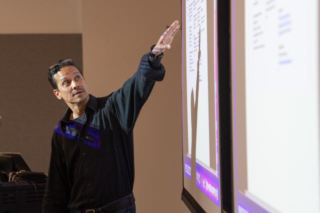 Education faculty member wearing black shirt pointing at screen.
