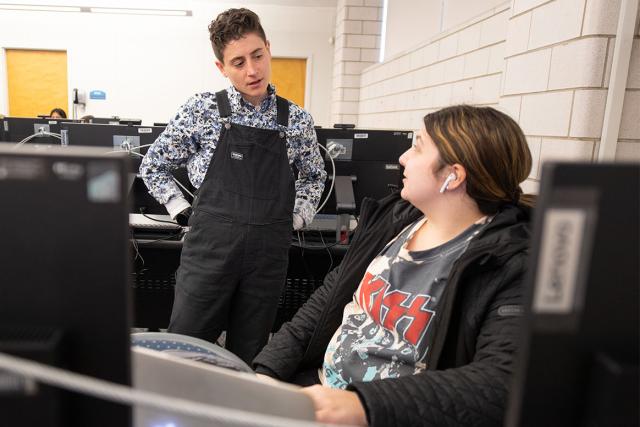 A Computer and Information Sciences professor talks to a student working in a computer lab.