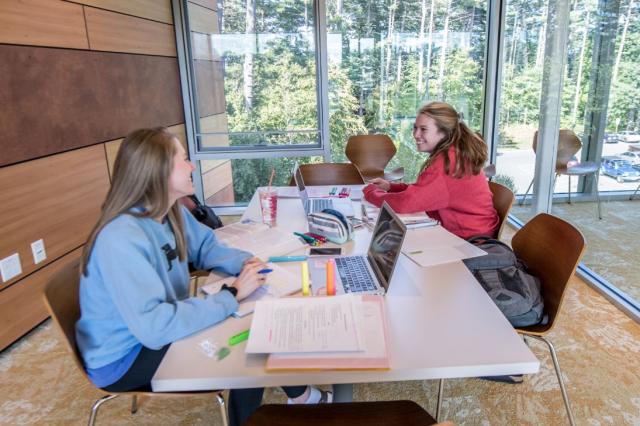 Two students spread their homework out on a large table in one of the study lounges inside University Hall.