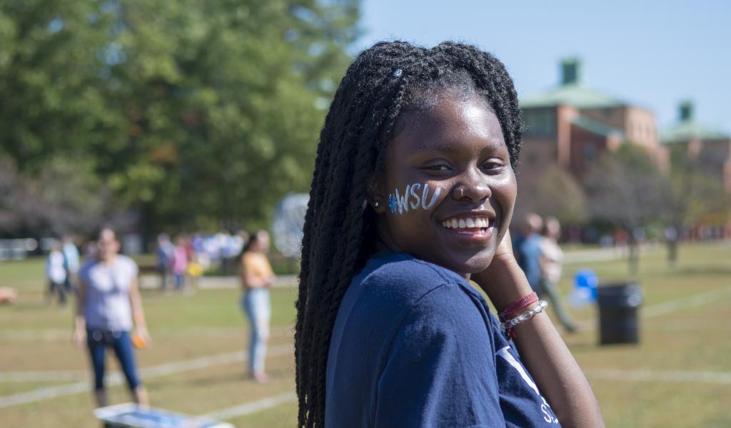 image of female student, with WSU face painting, smiling at the camera on the campus green